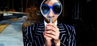 Person Using Magnifying Glass Enlarging The Appearance Of His Nose And Sunglasses